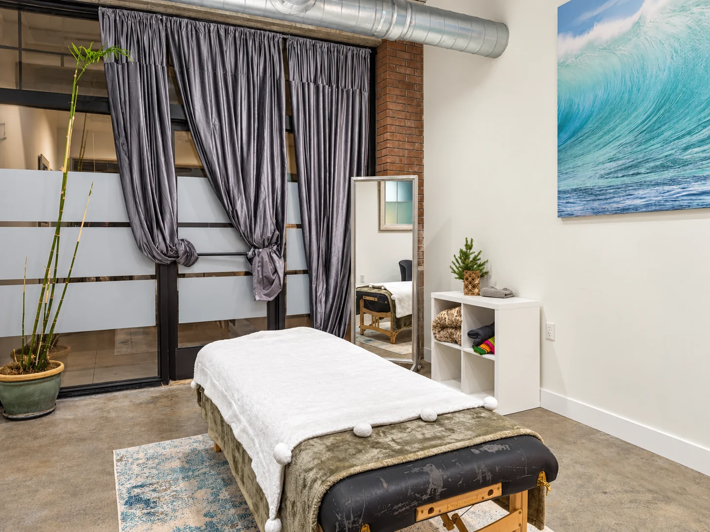 Treatment room with a white-covered massage table, gray curtains and ocean artwork at Elemntal Wellness