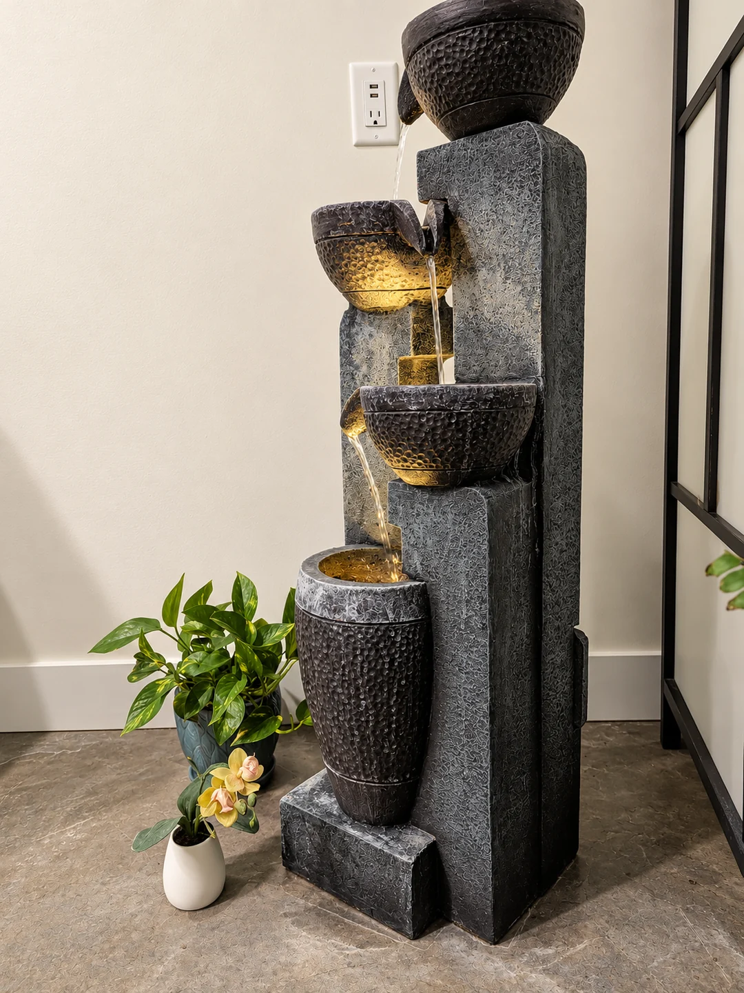 Tiered stone-look water fountain with illuminated bowls and potted plants at Elemntal Wellness