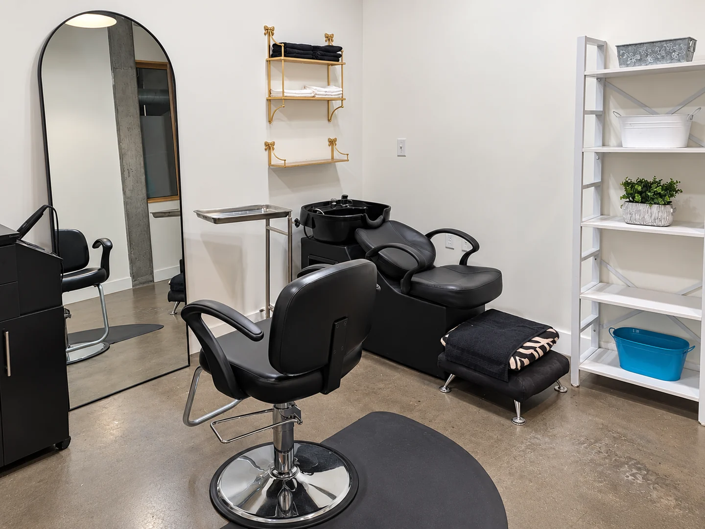 Hair studio with a black styling chair, arched mirror and shampoo basin at Elemntal Wellness