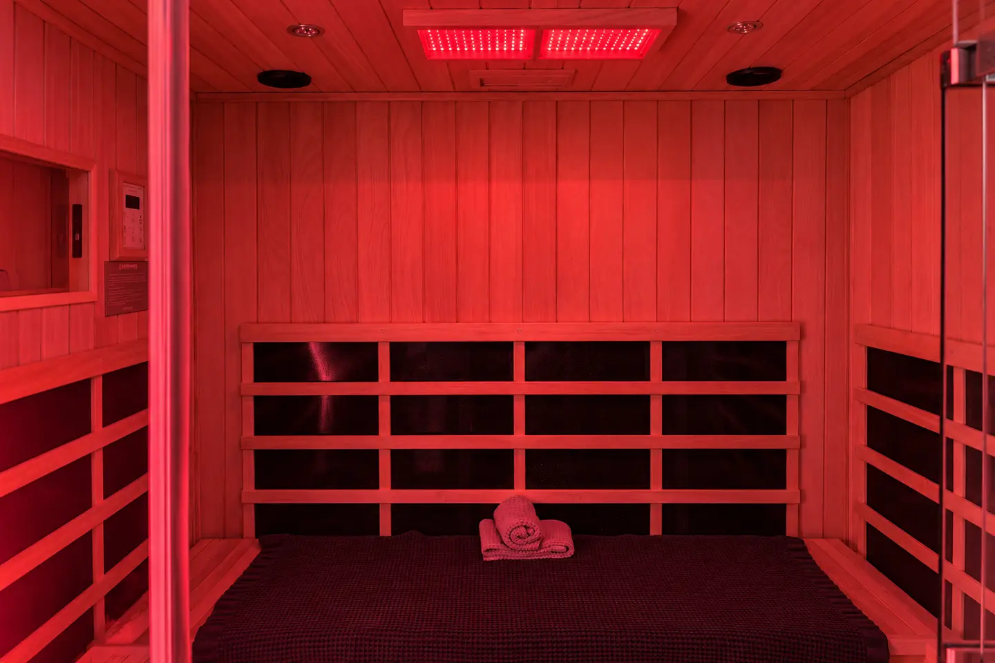 Red-lit infrared sauna with a wood bench and rolled towel at Elemntal Wellness