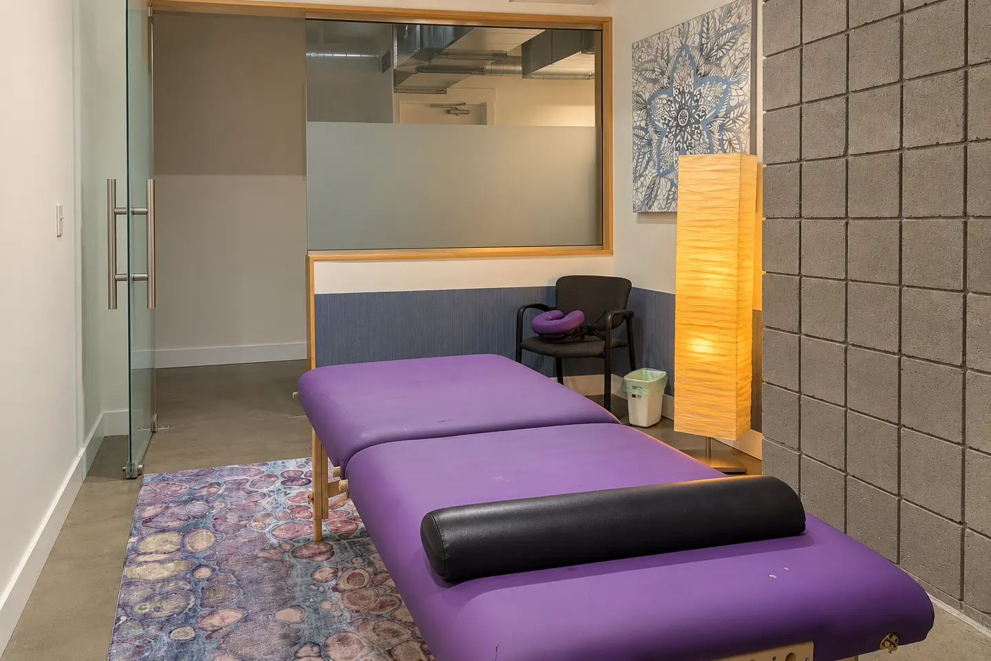 Massage room with a purple treatment table and warm floor lamp at Elemntal Wellness