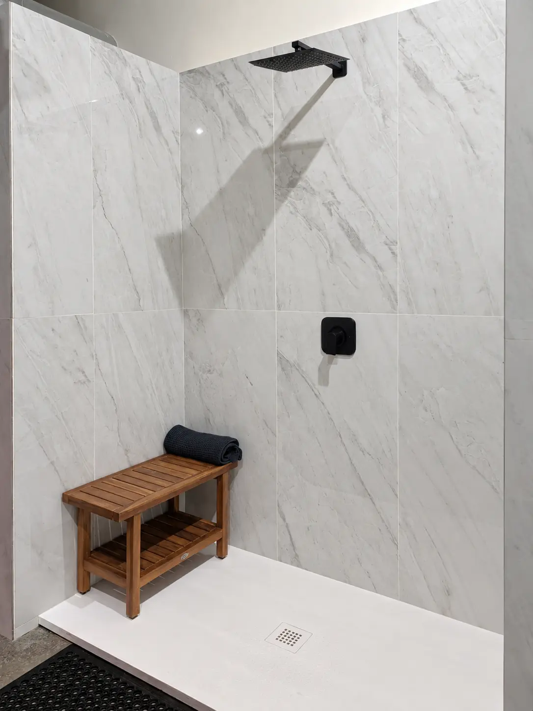 Rain shower with a black shower head, wood bench and rolled towel at Elemntal Wellness